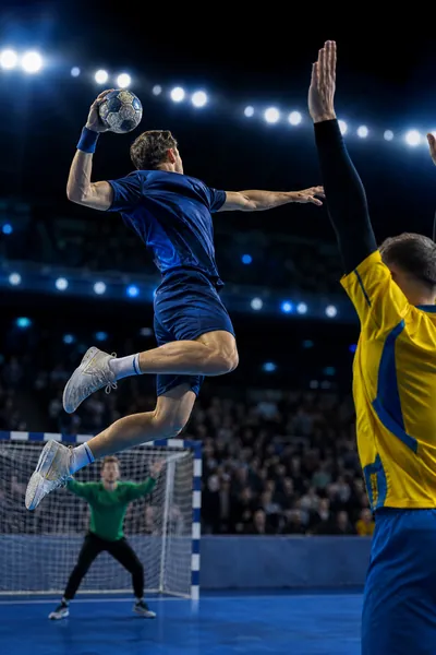 Handbollsspelare i blått och gult hoppar upp till skott i en inomhushall – handboll via bästa IPTV